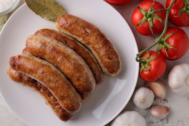 Foto salchichas a la plancha con variedad de verduras tomates y ajo sobre un fondo claro. vista superior