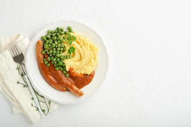 Salchichas y puré Salchichas a la parrilla con puré de patatas y guisantes verdes en un plato blanco sobre fondo claro Plato tradicional de Gran Bretaña e Irlanda Salchichas de ternera a la barbacoa Vista superior