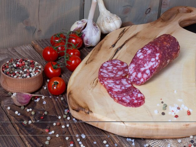 Salchichas en rodajas sobre una tabla de madera con ajo, tomates y pimienta Salchichas y especias sobre una mesa de madera antigua