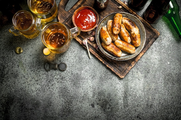 Salchichas en una sartén con una cerveza fría en la mesa rústica.