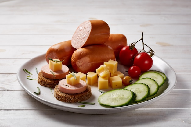 Salchichas con verduras y hierbas decorar con salsas y pan en un plato de cerámica gris sobre una mesa de madera blanca.