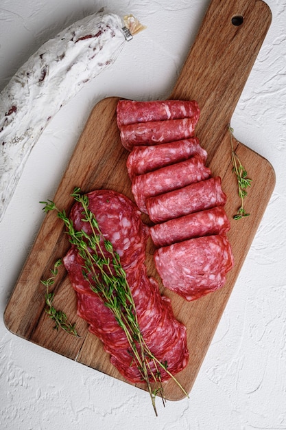 Salchichon ganze und geschnittene Schnitte, spanische Wurst auf weißer Oberfläche, flach gelegt.