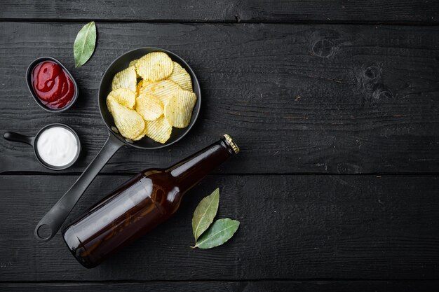 Salgadinho de batata frita e garrafa de cerveja na madeira preta