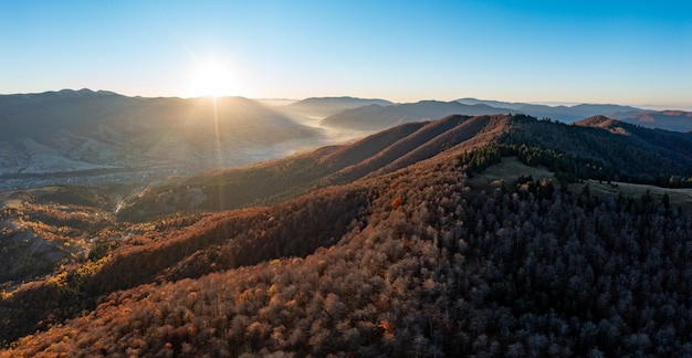 Salida del sol brillante en las altas montañas cubiertas de bosque de otoño