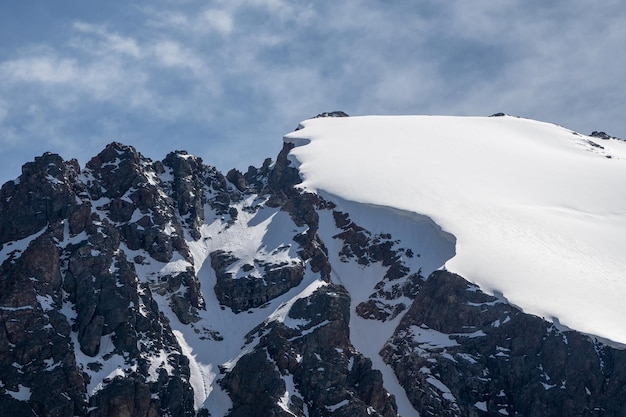 Saliência de neve no topo da montanha. Saliências das montanhas nevadas. Penhascos e grandes rochas. Terreno perigoso.