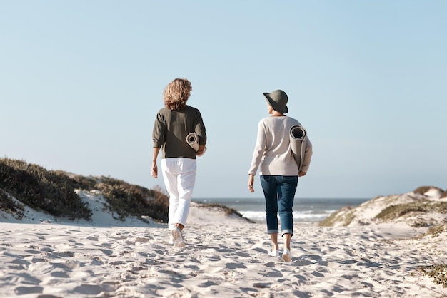 Saliendo a buscar el lugar perfecto Foto retrovisor de dos mujeres irreconocibles caminando con sus colchonetas en la playa