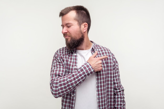 Salir Retrato de un hombre barbudo enojado con una camisa a cuadros casual que señala con el dedo hacia un lado y se da la vuelta luciendo irritado decepcionado con su estudio de comportamiento aislado en fondo blanco