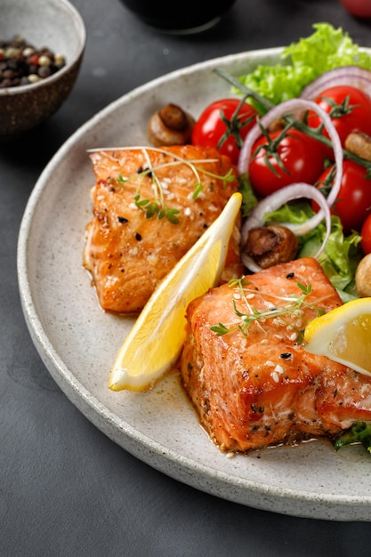 Salmão assado e salada de legumes fresca verde com tomate cereja cebola limão na placa cerâmica