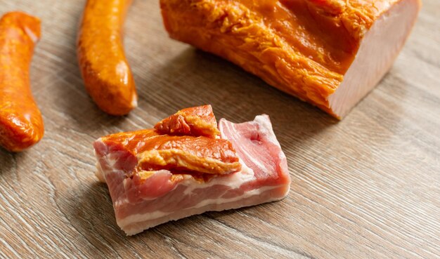 Foto salmão assado, porco cozido, salsicha e um pedaço de bacon numa mesa de madeira.