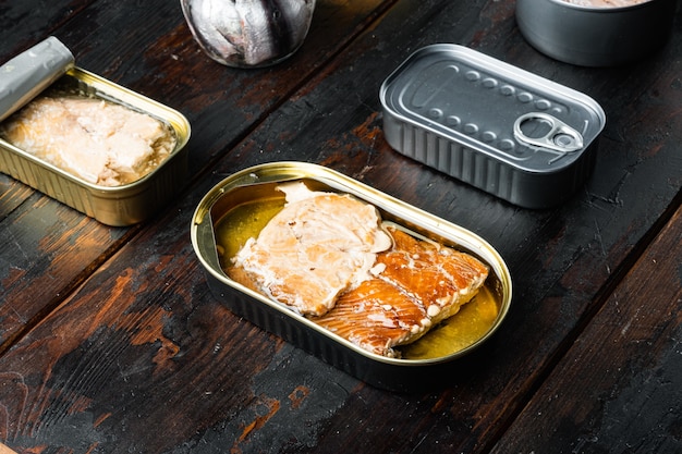 Foto salmão, atum, cavala truta e anchova - peixe enlatado em lata, na velha mesa de madeira escura