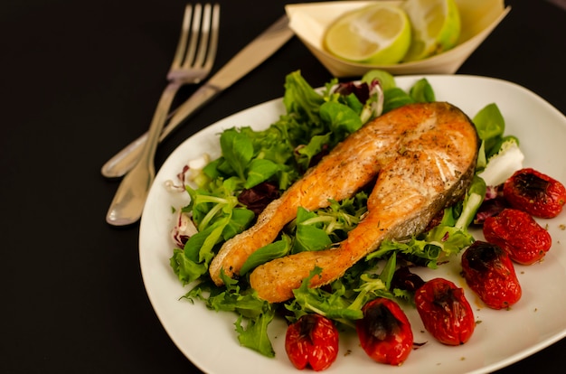 Foto salmão com tomate cereja assado e folhas de salada mista e metades de limão