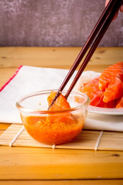 Salmão fresco com um pauzinho de madeira e mergulhado em uma tigela de molho de frutos do mar