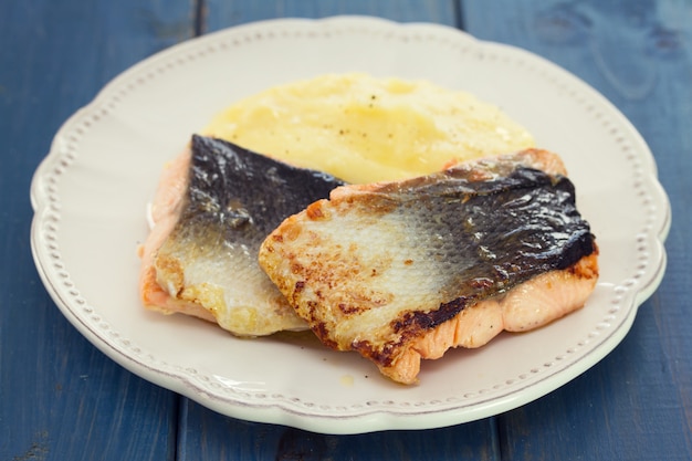 Salmão frito com purê de batatas no prato branco sobre madeira azul