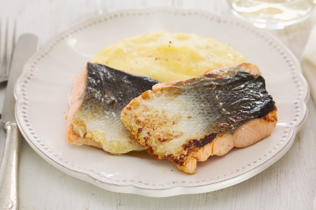 Salmão frito com purê de batatas no prato branco sobre madeira branca