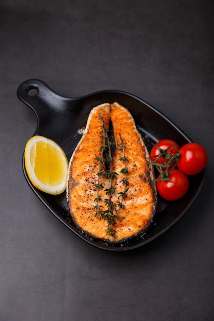 Salmão grelhado com tomate cereja tomilho e limão em uma pequena grelha preta peixe frito é um prato tradicional de comida caseira e restaurantes closeup de foco seletivo de fundo preto