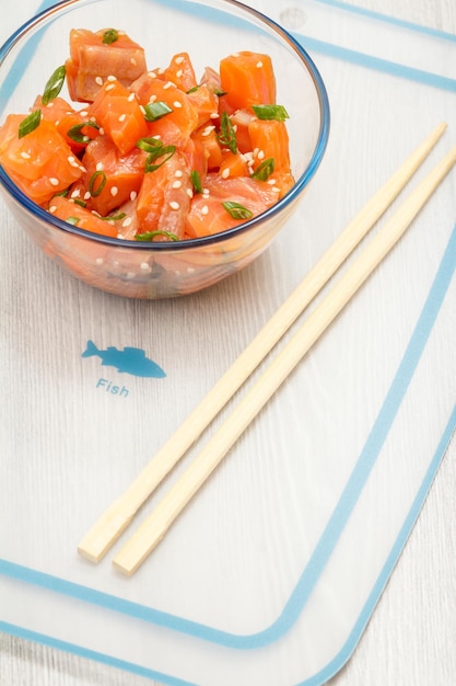 Salmão havaiano cutucar com cebolinha e sementes de gergelim em tigela de vidro com pauzinhos Vista superior