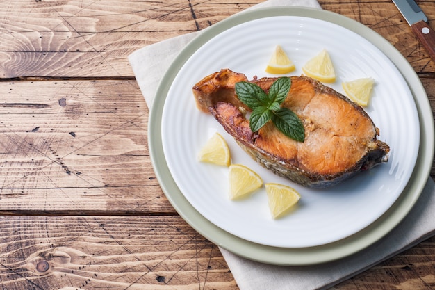 Salmões cozidos bife dos peixes em uma placa com limão. Mesa de madeira.