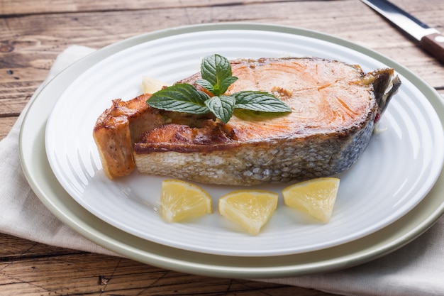 Salmões cozidos bife dos peixes em uma placa com limão. mesa de madeira.