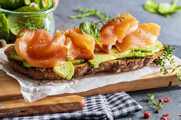 Salmón ahumado apetitoso y saludable con aguacate y verduras (brotes de espinaca, tomate, tomillo) sobre tostadas. Aspecto casero.