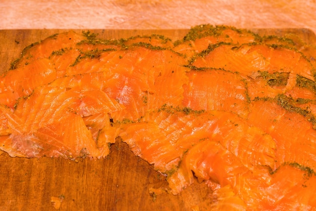 Salmón ahumado artesanal cubierto de eneldo y especias sobre una tabla de madera.