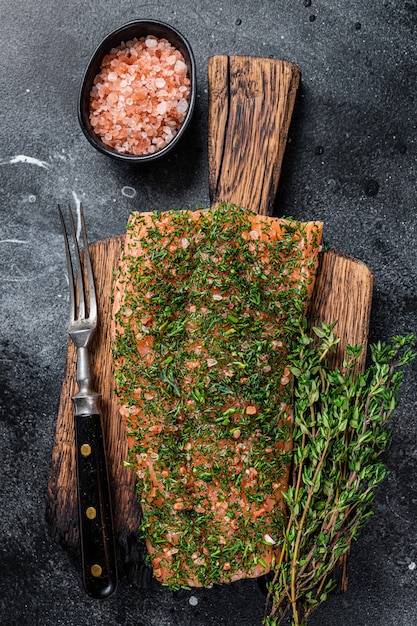 Salmón curado Gravlax con eneldo y sal sobre tabla de madera. Fondo negro. Vista superior.