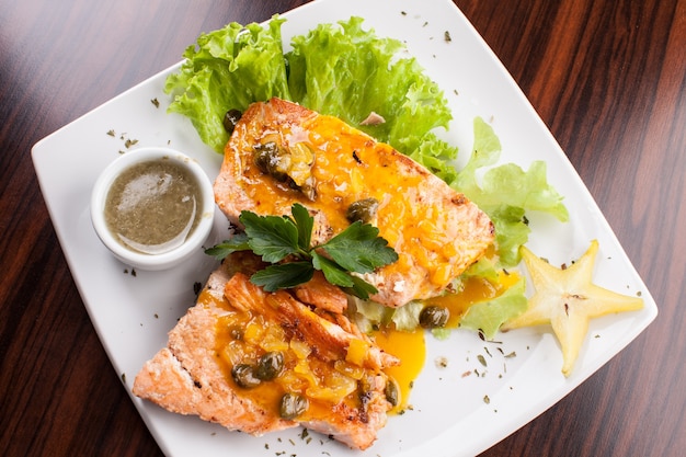 Salmón con ensalada, carambola con salsa de alcaparras en mesa de madera