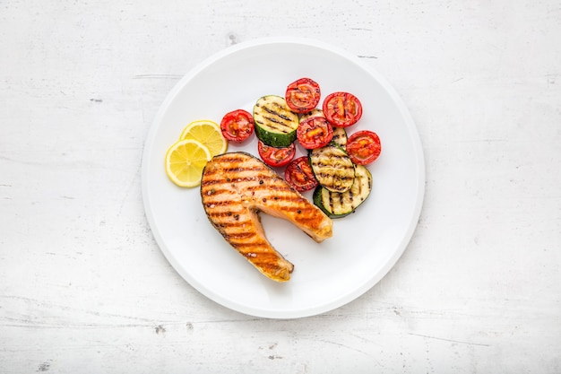 Salmón. Filete de salmón a la plancha con tomate y calabacín en un plato blanco.