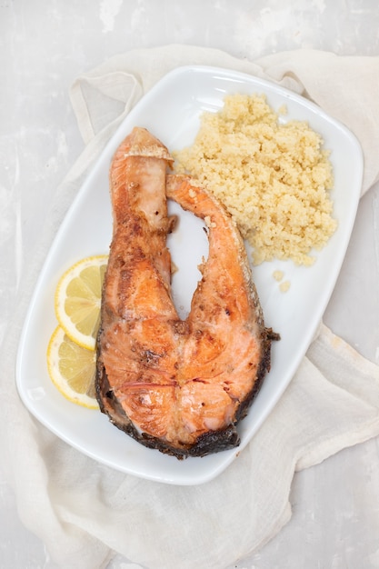 Salmón frito con cous cous y limón en plato blanco