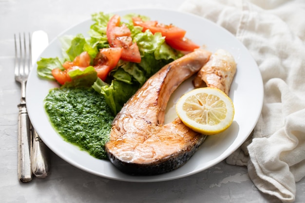 Salmón frito con espinacas, limón y ensalada en plato blanco