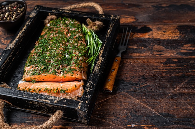 Salmón Gravlax curado con eneldo y sal en bandeja de madera. Fondo de madera oscura. Vista superior.