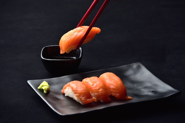 Salmón nigiri sushi y salsa de wasabi con palillos en negro valvet.