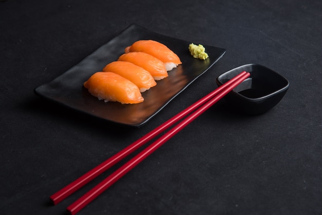 Salmón nigiri sushi y salsa de wasabi con palillos en terciopelo negro.