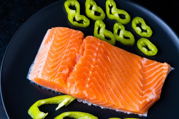 Foto salmón de pescado salado con pimienta y cebolla en un plato negro. vista superior. espacio libre para su texto.