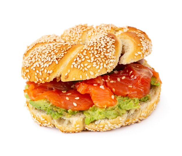 Salmón en rodajas con aguacate en bagel con semillas de sésamo aislado sobre fondo blanco.