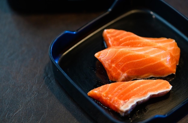 Foto salmón en rodajas sobre plato negro y fondo negro comida japonesa