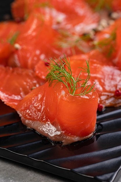 Salmón salado ligeramente salado cortado en rodajas en un plato negro con especias Carne roja pescado merienda nutritiva restaurante omega que sirve pescado con especias y eneldo