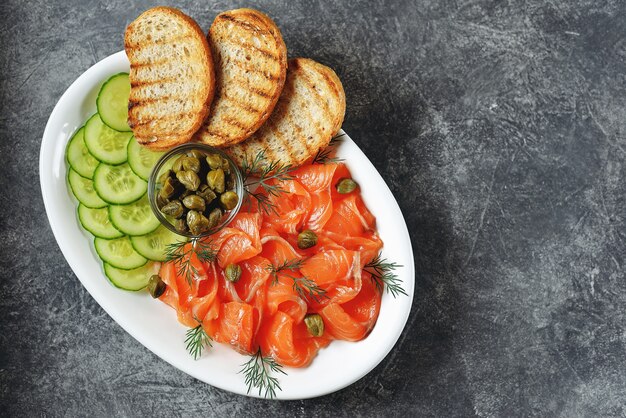 Salmón salado, pepino, alcaparras, eneldo y pan a la plancha