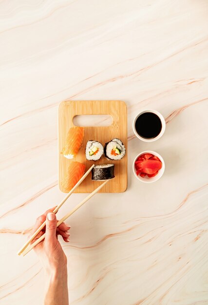 Salmón de sushi en tabla de cortar de madera. Mano de mujer sosteniendo sushi roll con chipsticks. Endecha plana