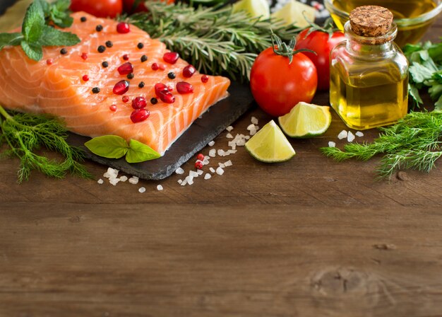 Salmón con verduras, aceite de oliva y hierbas en madera de cerca con espacio de copia