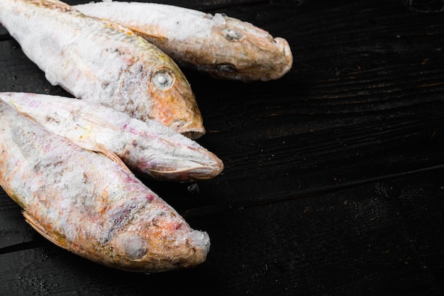 Salmonete congelado o pescado sultanka, sobre fondo de mesa de madera negra, con espacio para copiar texto