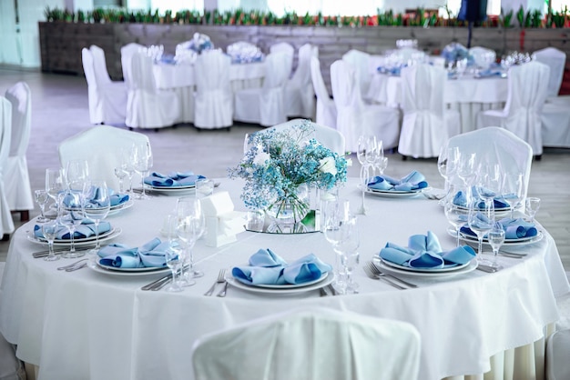 El salón de banquetes con mesas redondas. Restaurante salón de banquetes con mesas de boda decoradas servidas. Mesa redonda blanca con elegantes composiciones de flores frescas.