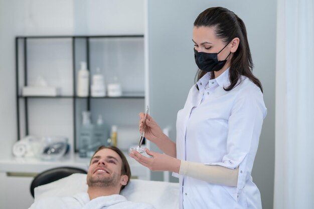 Salón de belleza. Cosmetóloga aplicando máscara facial a la cara del hombre