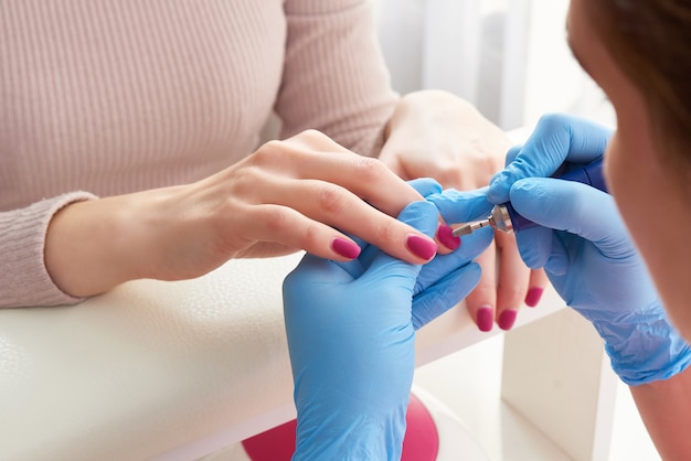 Salón de esteticista, manicura, procedimiento de esmalte de uñas. Manicura de hardware profesional con máquina eléctrica en salón de belleza. El maestro usa una máquina eléctrica para quitar el esmalte de uñas de las manos durante la manicura.