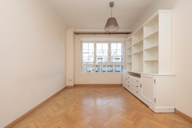 Salón con librería de madera lacada en blanco junto a la ventana con suelo de parquet en espiga