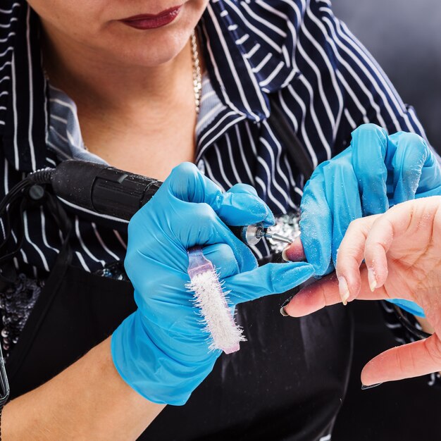 Salón de manicura, manos del cliente y primer plano maestro. Tratamiento de uñas con cortador.