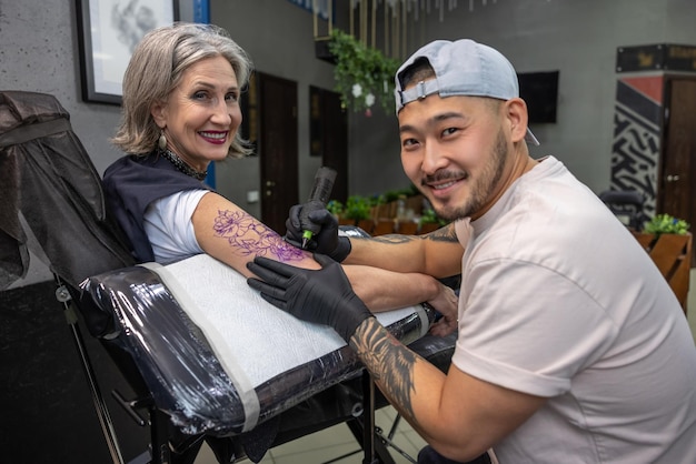 En el salón de tatuajes. Tatuaje maestro dibujo tatuaje en el brazo de la mujer