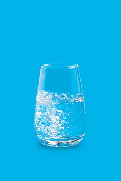 Salpicaduras de agua clara con burbujas en un solo vaso contra un azul vibrante brillante