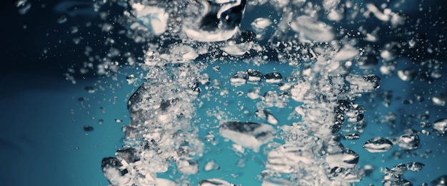 Salpicaduras de agua y cubitos de hielo Salpicaduras de hielo en un vaso de agua Vertiendo cubitos de hielo bajo el agua cayendo en un fondo de riego claro Refrescante bebida helada Hielos en un vaso con fondo azul