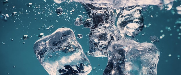 Foto salpicaduras de agua y cubitos de hielo salpicaduras de hielo en un vaso de agua vertiendo cubitos de hielo bajo el agua cayendo en un fondo de riego claro refrescante bebida helada hielos en un vaso con fondo azul