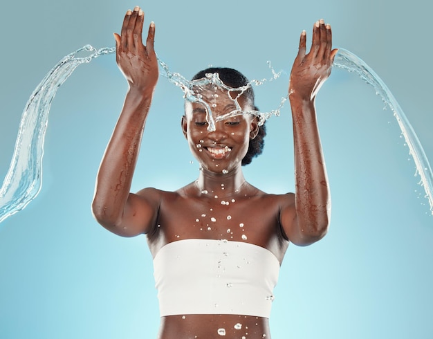 Salpicaduras de agua y mujer negra lavándose sobre un fondo de estudio azul para higiene y aseo Limpieza limpia y cuidado corporal o cuidado de la piel para mujeres afroamericanas duchándose por belleza y bienestar